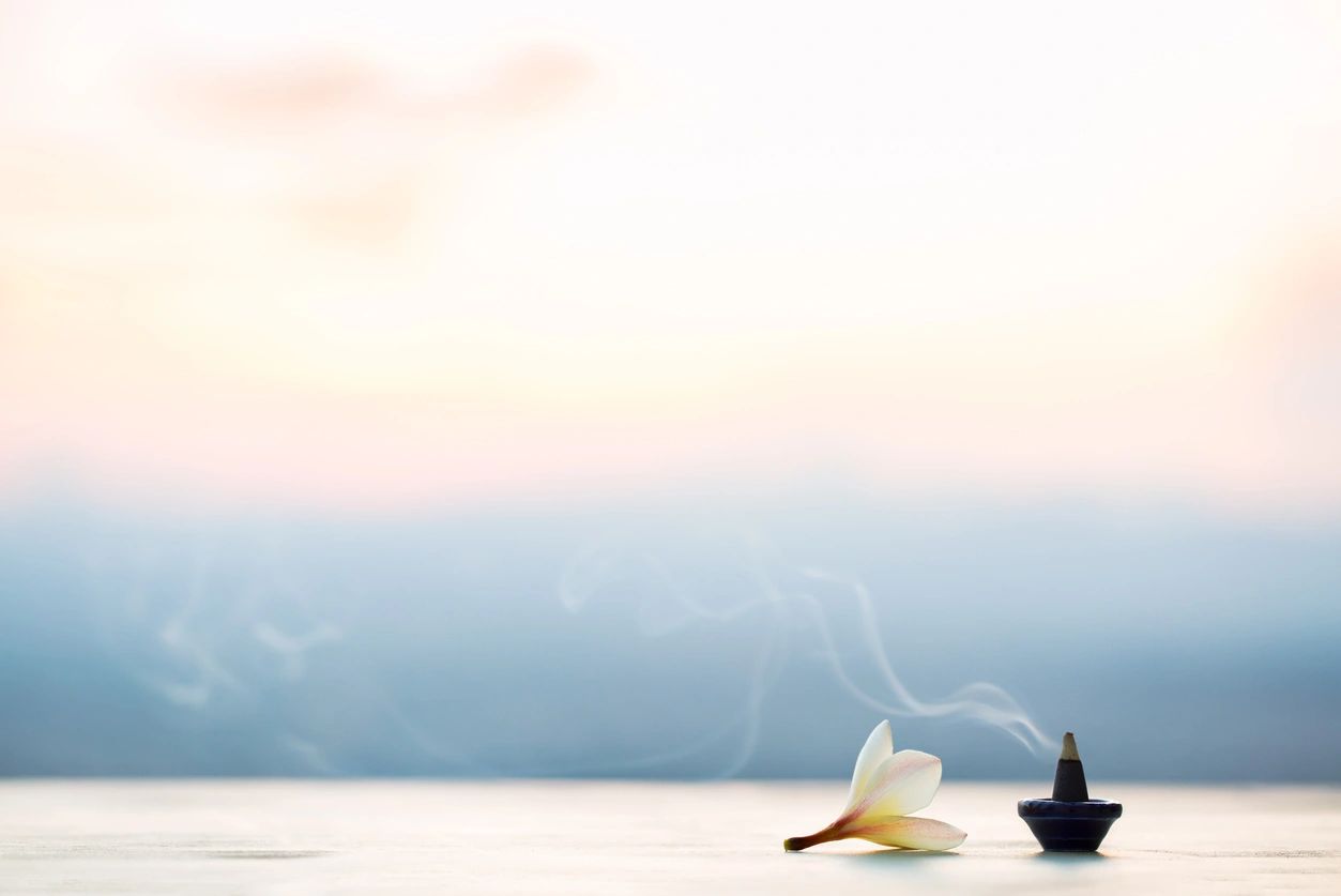 A serene scene with a lotus flower and incense smoke by calm water at sunset.